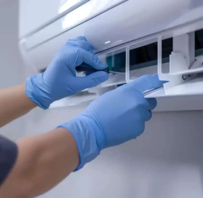 A technician wearing blue gloves cleaning or maintaining an air conditioning unit