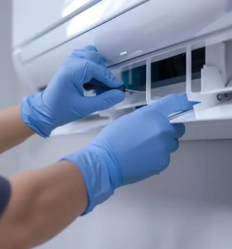 A technician wearing blue gloves cleaning or maintaining an air conditioning unit