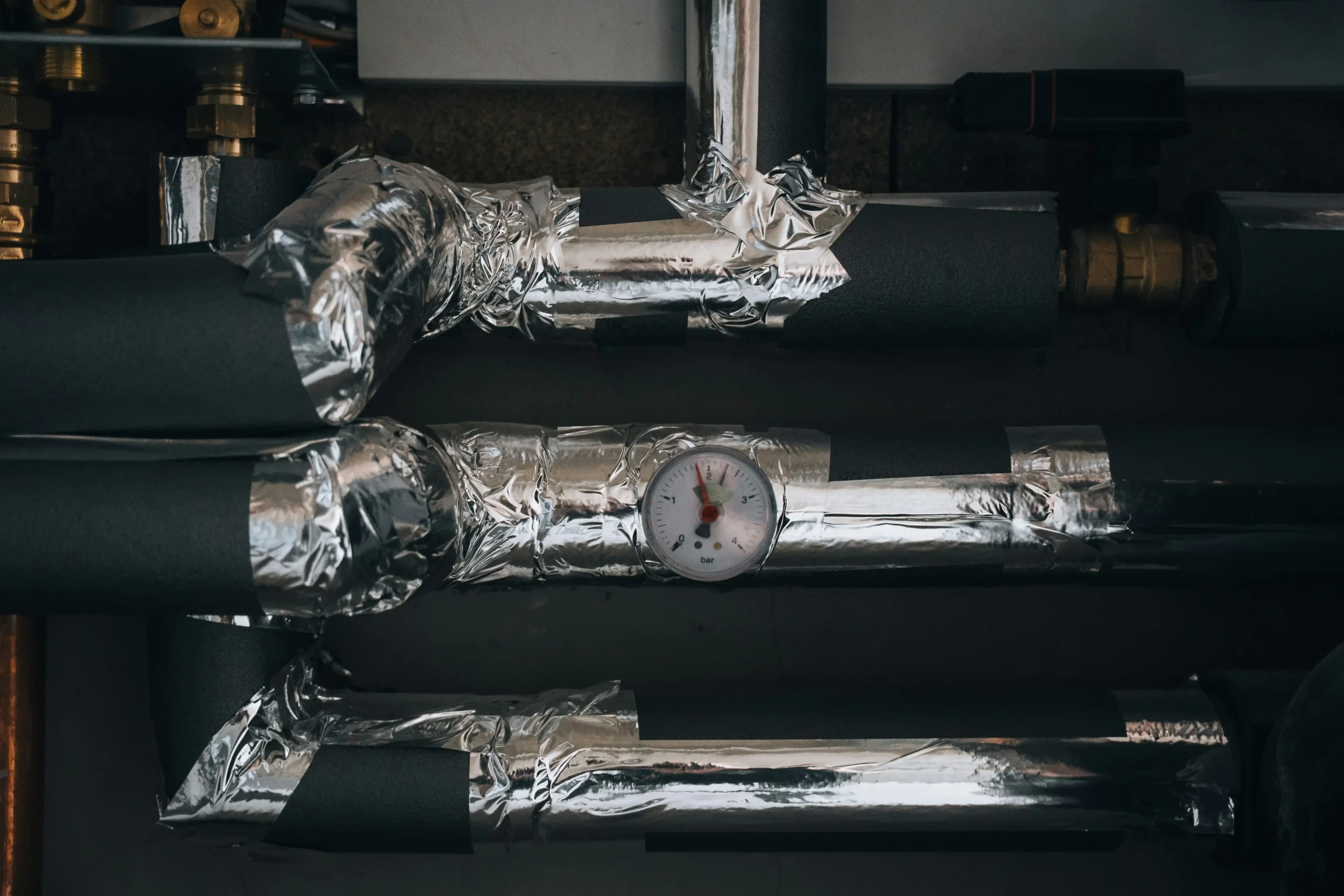 Close-up of insulated pipes with a pressure gauge, wrapped in metallic tape for protection.