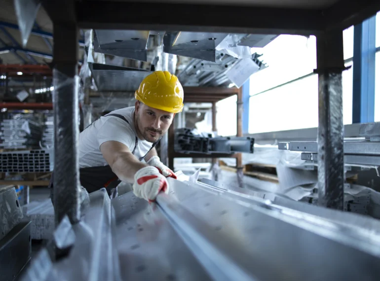 A worker carefully handling metal components in a manufacturing facility, preparing customized kitchen equipment and appliances for restaurant renovations and food service setups.