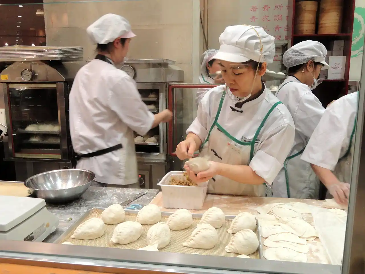 Chefs working in a bakery, preparing dough and filling in a kitchen with baking equipment in the background.