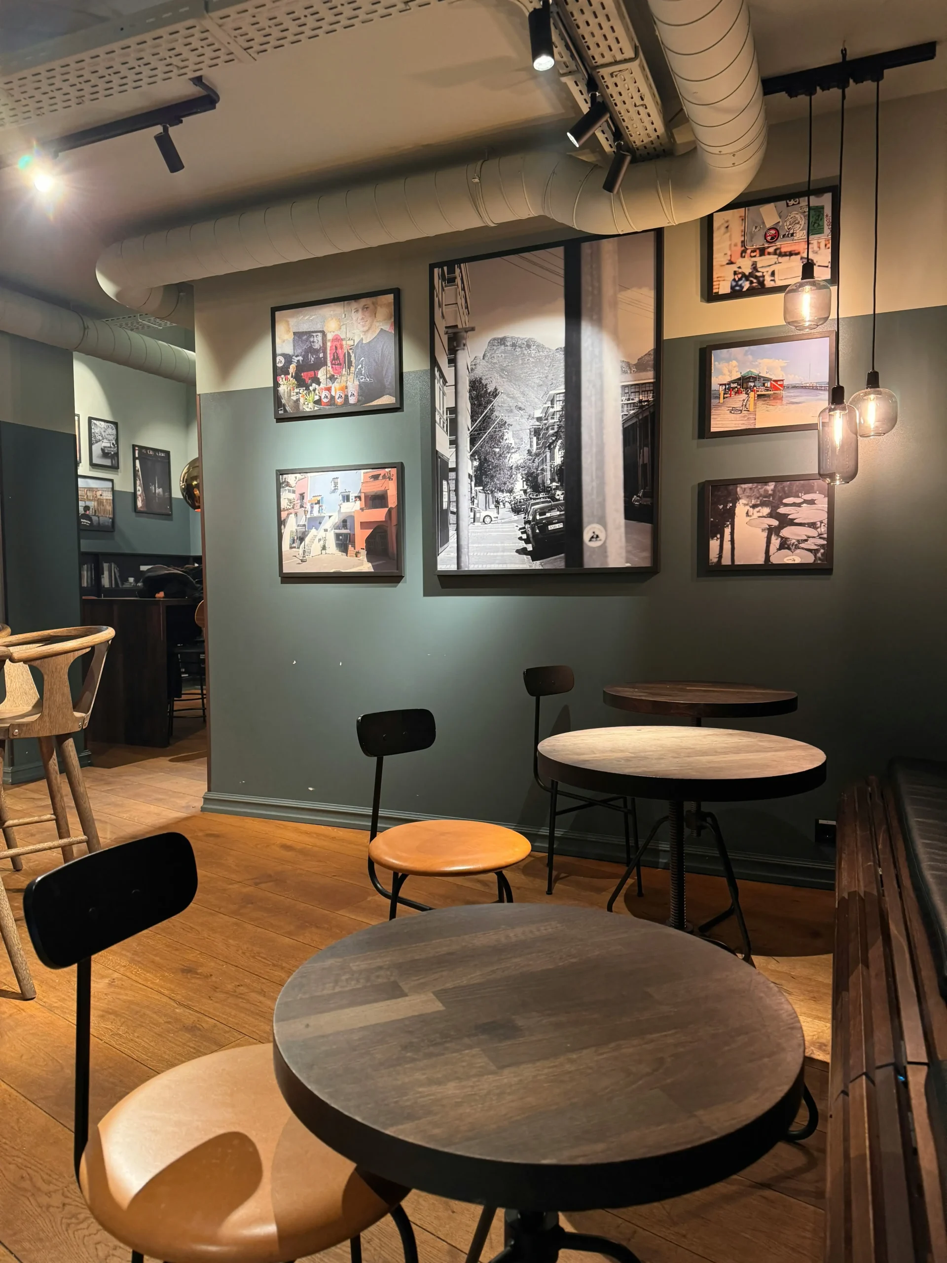 A modern café setting with minimalistic furniture, illuminated by pendant lights, and decorated with black-and-white photographs, creating a relaxed and stylish atmosphere for diners.