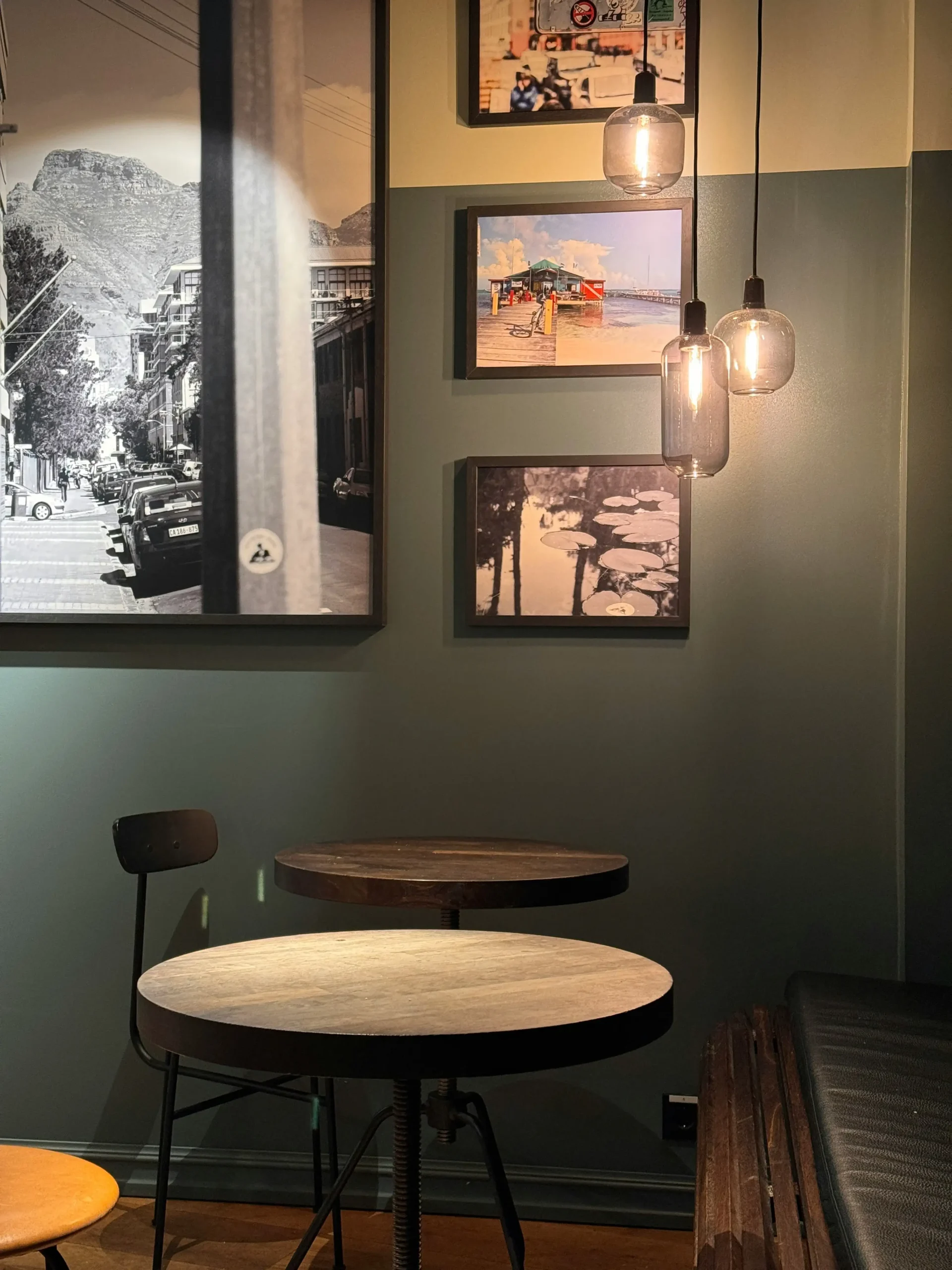A modern café setting with minimalistic furniture, illuminated by pendant lights, and decorated with black-and-white photographs, creating a relaxed and stylish atmosphere for diners.