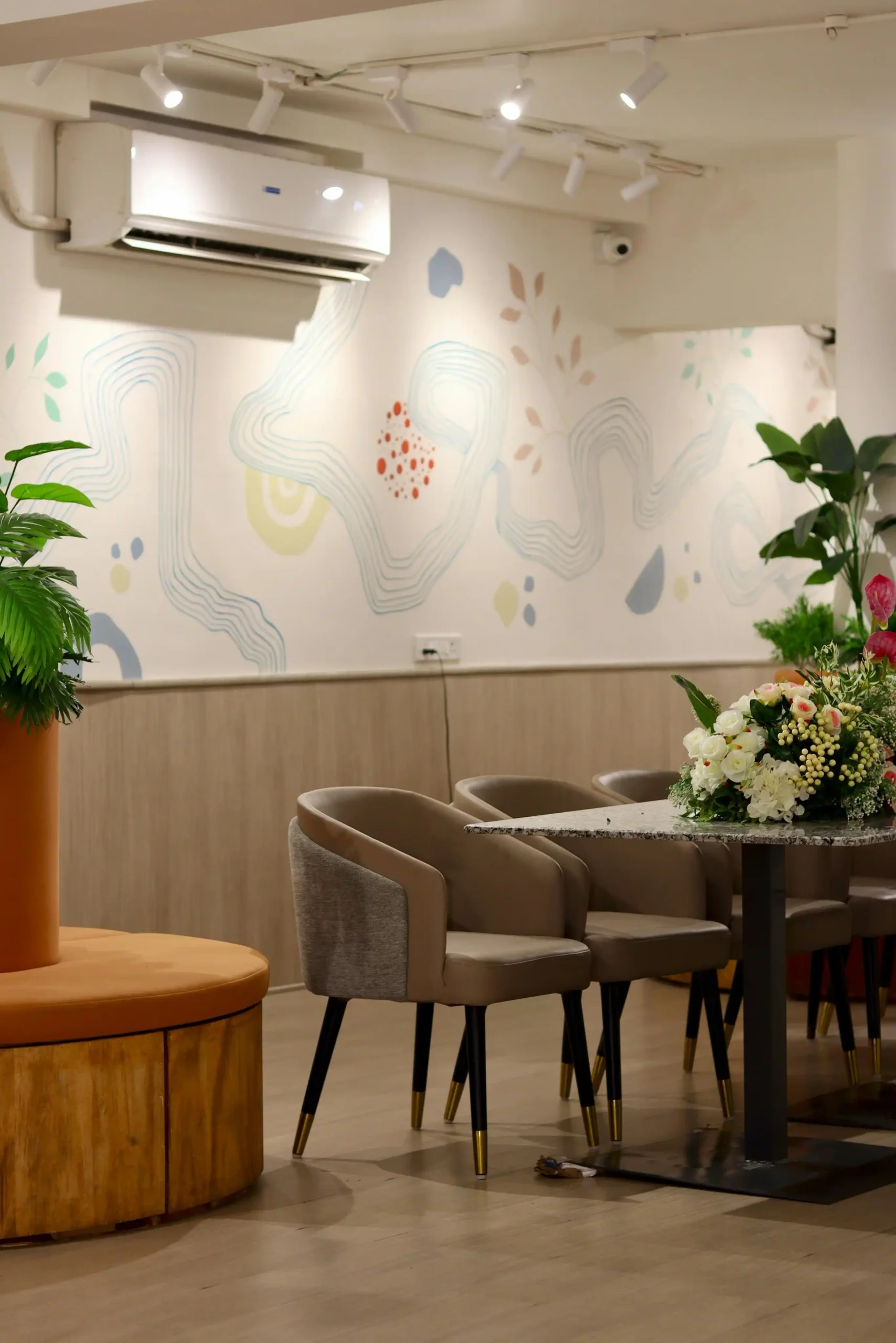 Cozy and modern restaurant interior with artistic wall design, comfortable seating, and fresh flowers on the table.