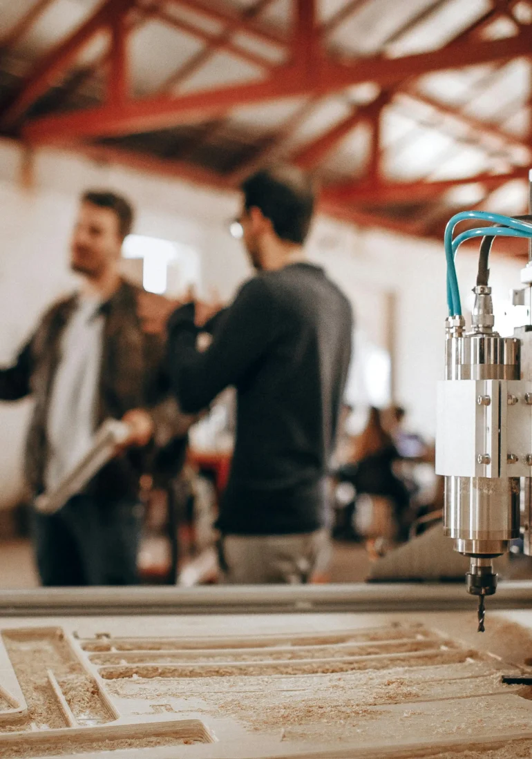 A team of professionals discussing plans while a CNC machine is actively working on a restaurant kitchen equipment project, highlighting the precision and technology used in custom restaurant renovations.