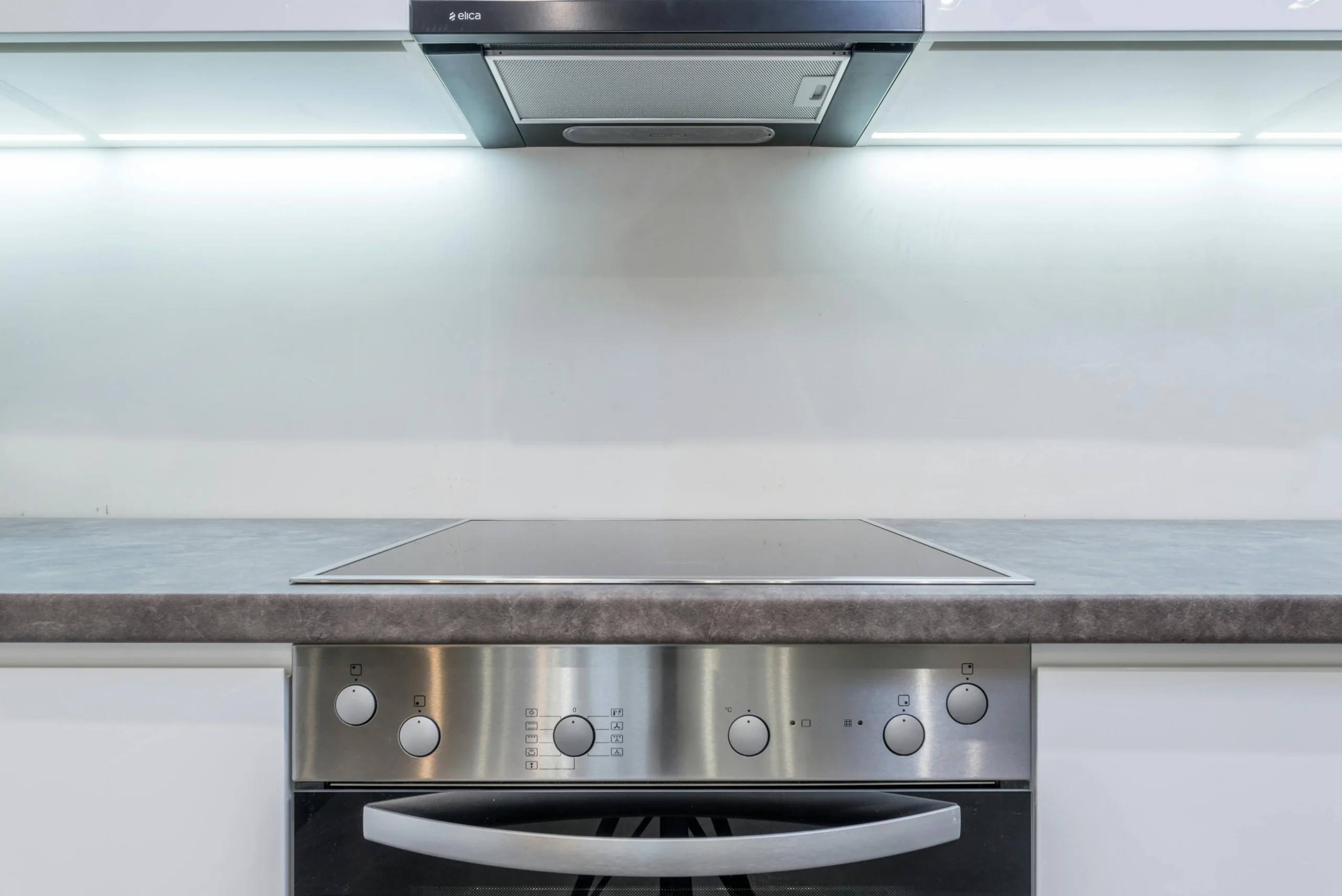 A clean and modern kitchen countertop featuring a stainless steel stove, oven, and range hood with soft under-cabinet lighting.