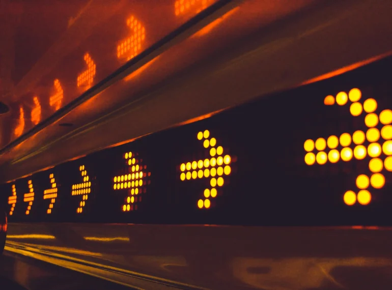 Close-up of a row of illuminated orange arrows on a LED display, indicating direction.