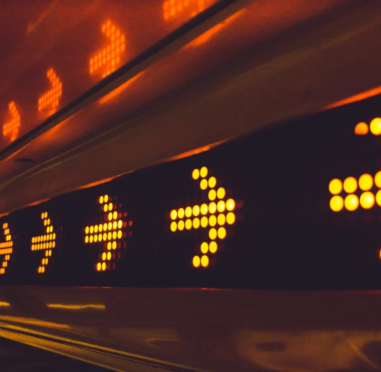 Close-up of a row of illuminated orange arrows on a LED display, indicating direction.