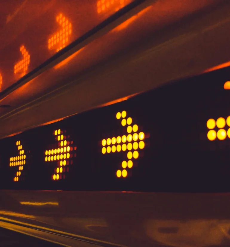 Close-up of a row of illuminated orange arrows on a LED display, indicating direction.