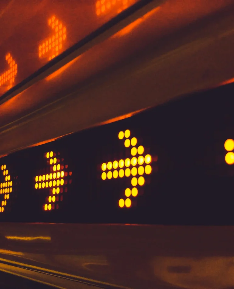 Close-up of a row of illuminated orange arrows on a LED display, indicating direction.