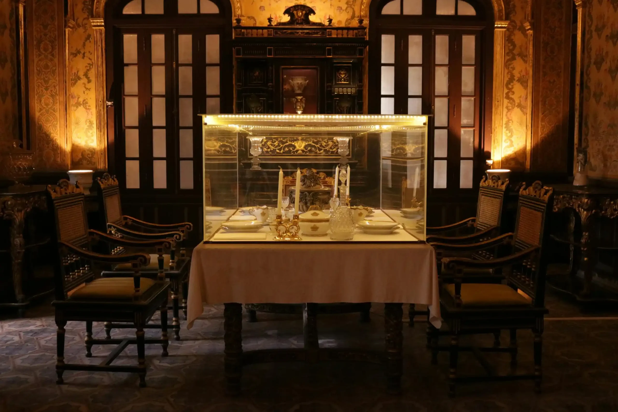 Elegant dining setup inside a vintage room with ornate chairs, a glass display case, and decorative tableware.