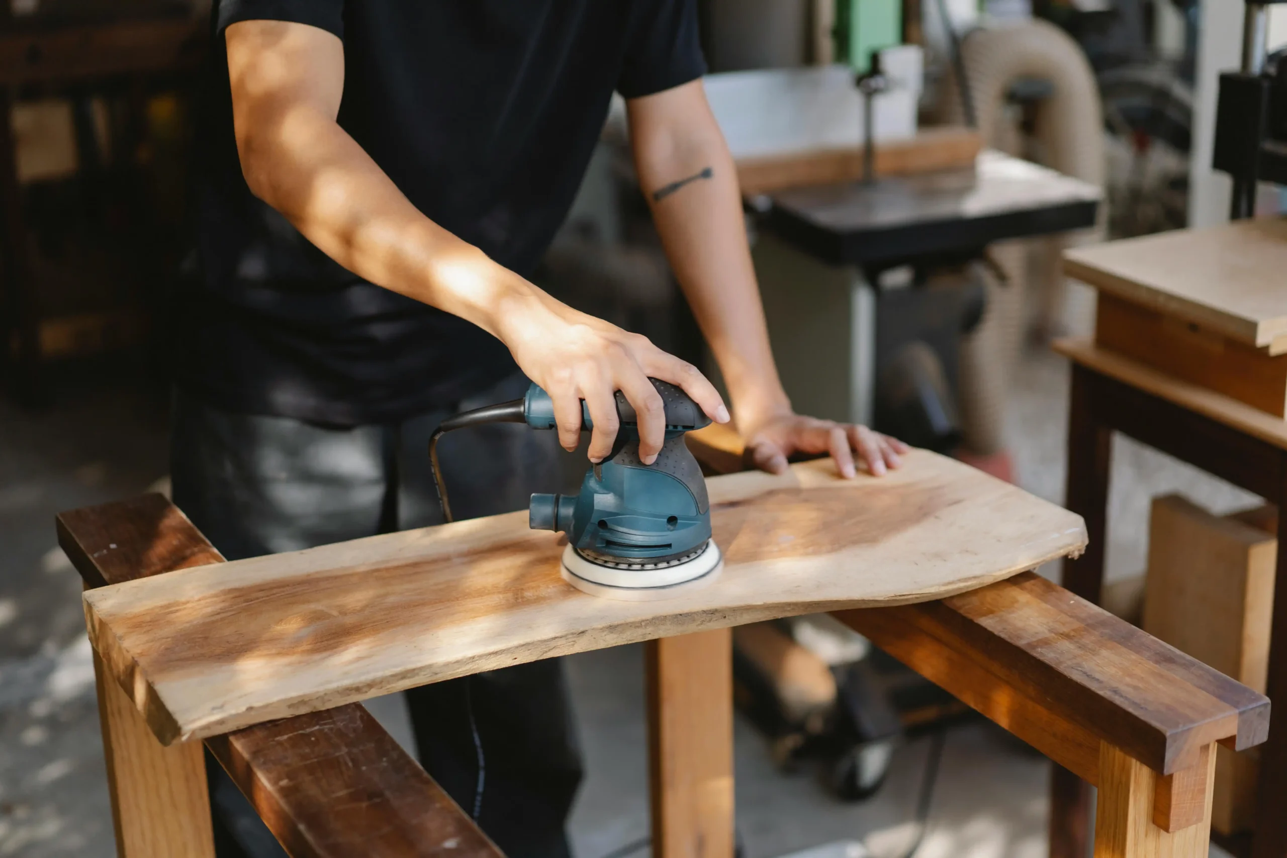 A skilled craftsman using a sander to smooth the surface of a wooden piece, preparing it for use in custom restaurant furniture, ensuring a polished and professional finish.