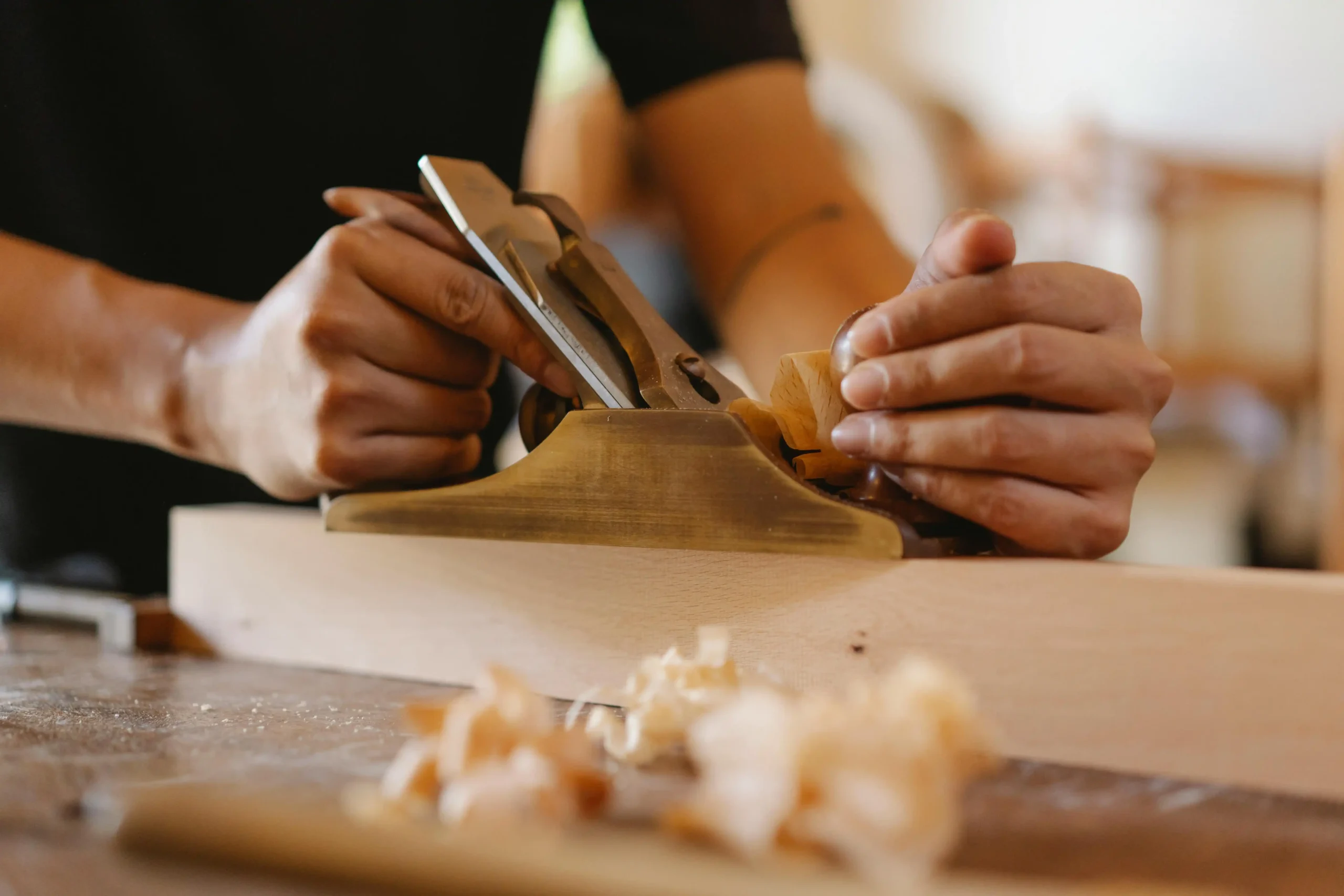 A skilled artisan using a wood plane to shape and smooth a wooden piece, perfecting the texture and finish for custom restaurant furniture construction.