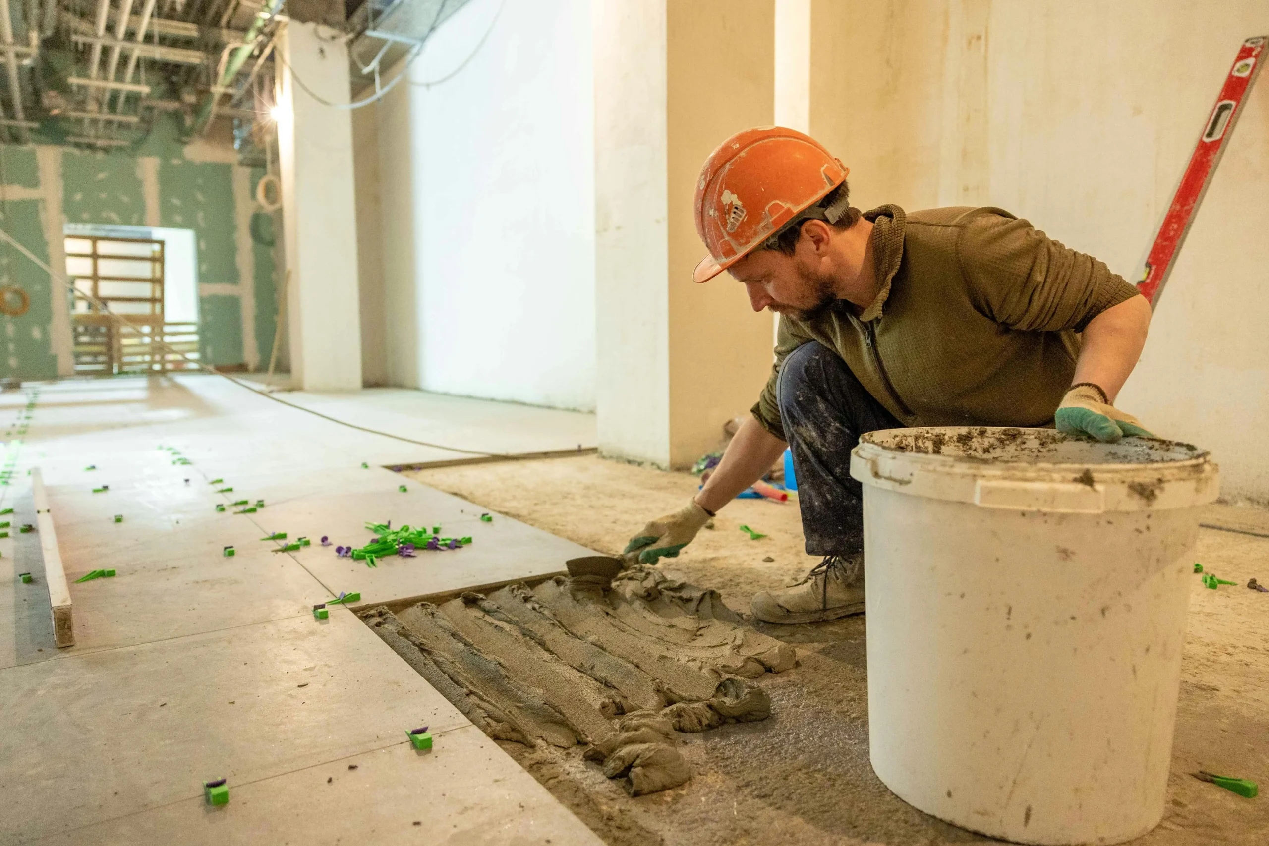 A construction worker carefully applying adhesive to the floor in a restaurant renovation project, preparing for new flooring installation to enhance the dining space.