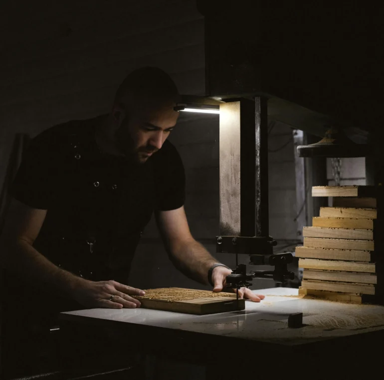 A skilled craftsman working with a press machine to shape wooden pieces, essential for creating custom furniture and fixtures for restaurant interiors.