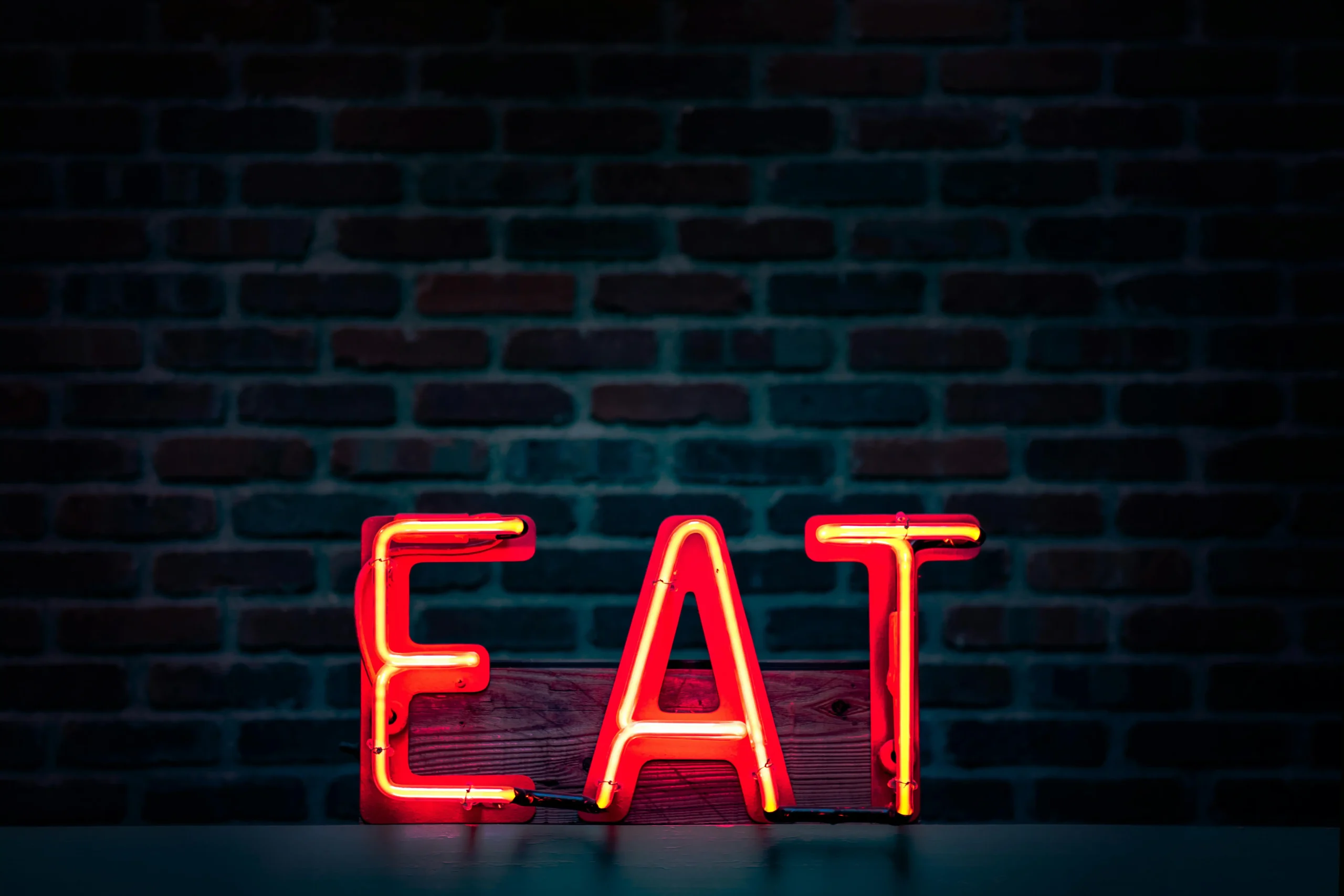 A neon "EAT" sign glowing in bright red against a brick wall backdrop
