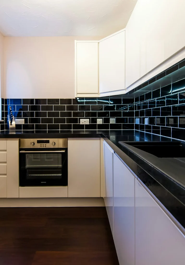 A contemporary restaurant kitchen featuring black tiled walls, white cabinetry, and stainless steel appliances, perfect for stylish and functional food preparation spaces.