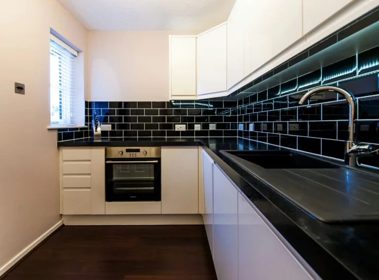 A contemporary restaurant kitchen featuring black tiled walls, white cabinetry, and stainless steel appliances, perfect for stylish and functional food preparation spaces.
