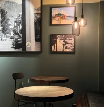 A modern café setting with minimalistic furniture, illuminated by pendant lights, and decorated with black-and-white photographs, creating a relaxed and stylish atmosphere for diners.